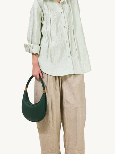 Emerald green pebbled leather Luna Bag with gold hardware, worn with light green blouse and beige pants.