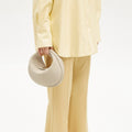 Luna Bag in ivory pebbled leather held by a model wearing a yellow shirt and trousers.
