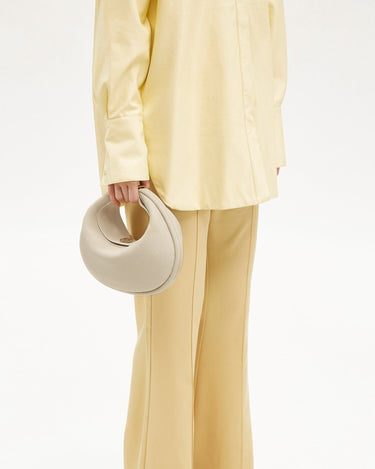 Luna Bag in ivory pebbled leather held by a model wearing a yellow shirt and trousers.