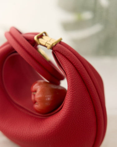 Luna Bag in Lucky Red pebbled leather with brass clasp, featuring a unique curved design.