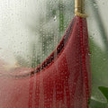 Luna Bag in Lucky Red with golden hardware detail, visible through a wet glass surface.