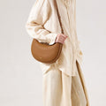 Brown full-grain leather Luna Bag with adjustable strap, worn by a model in beige linen.