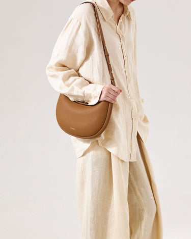 Brown full-grain leather Luna Bag with adjustable strap, worn by a model in beige linen.