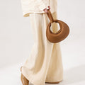 Brown full-grain leather Luna bag with gold clasp, held by person in linen outfit.