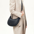 Onyx Luna Bag in pebbled leather worn crossbody by a woman in a tan suit.