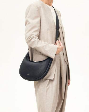 Onyx Luna Bag in pebbled leather worn crossbody by a woman in a tan suit.