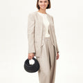 Black Luna Bag with gold clasp held by woman in beige suit. Premium leather handbag.