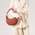 Luna Bag in Oolong pebbled leather with gold hardware, held by a model in linen clothing.
