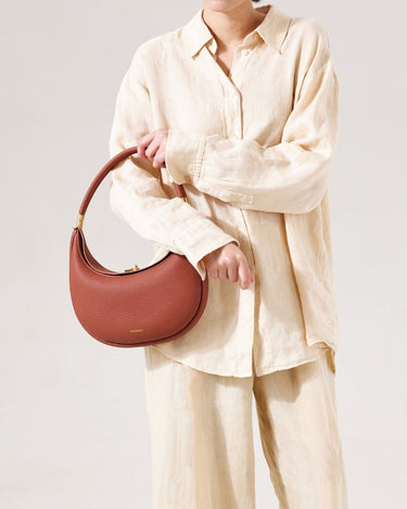 Luna Bag in Oolong pebbled leather with gold hardware, held by a model in linen clothing.