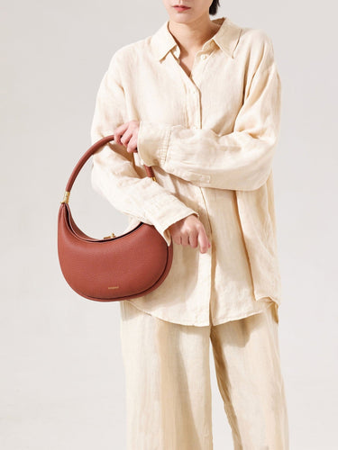 Luna Bag in Oolong pebbled leather with gold hardware, held by a model in linen clothing.