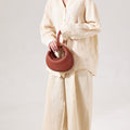 Oolong Luna Bag with curved handles, crafted from pebbled leather, held by a model in a cream linen outfit.