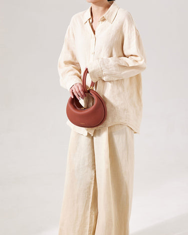 Oolong Luna Bag with curved handles, crafted from pebbled leather, held by a model in a cream linen outfit.