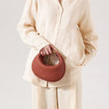 A person holds a brown pebbled leather Luna Bag with gold hardware.