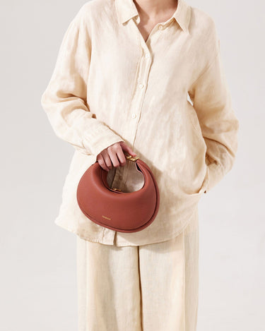 A person holds a brown pebbled leather Luna Bag with gold hardware.