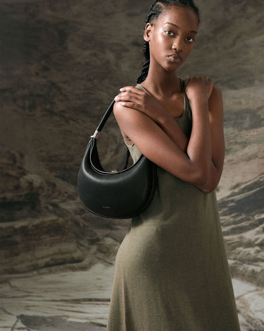 Luna Bag in Onyx black full-grain leather with silver-tone hardware, worn by a model in an olive-green dress.