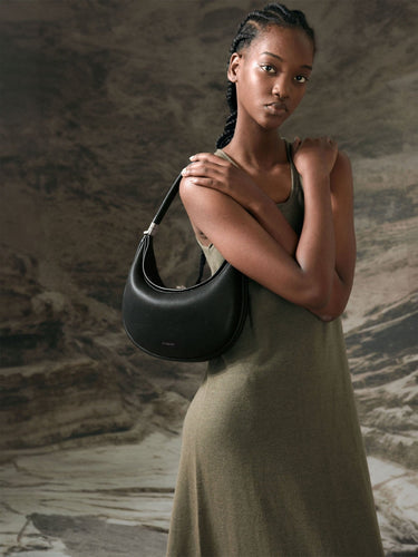 Luna Bag in Onyx black full-grain leather with silver-tone hardware, worn by a model in an olive-green dress.