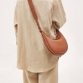 A person wearing a neutral-toned outfit carries the Luna Bag in eco caramel vegan leather crossbody.