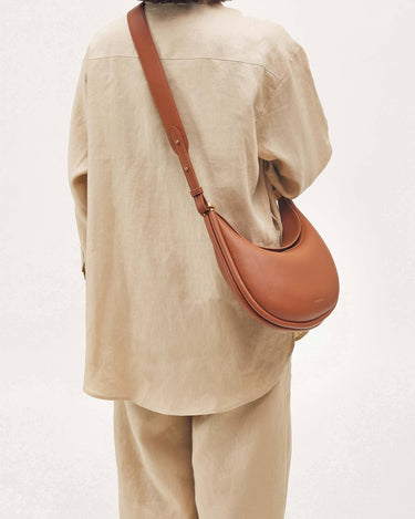 A person wearing a neutral-toned outfit carries the Luna Bag in eco caramel vegan leather crossbody.