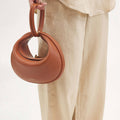 Luna Bag in Eco Caramel vegan leather with a gold clasp, held by a person in beige linen clothing.