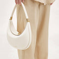 White vegan leather Luna Bag with gold hardware, held by a person wearing beige linen pants and a light-colored top.