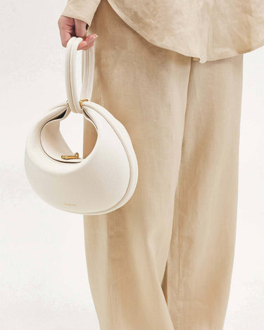 White vegan leather Luna Bag with gold clasp, held by hand. Made from recycled materials.