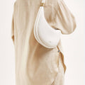 White vegan leather Luna Bag with gold hardware worn on the shoulder by a person in a beige linen outfit.