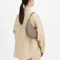 Taupe full-grain leather Luna bag with gold buckle, worn cross-body by a woman.