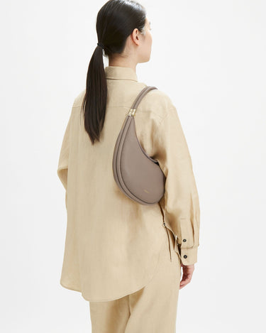 Taupe full-grain leather Luna bag with gold buckle, worn cross-body by a woman.