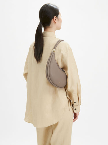 Taupe full-grain leather Luna bag with gold buckle, worn cross-body by a woman.