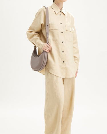 Luna Bag in grey full-grain leather with adjustable strap, worn with a tan linen outfit.