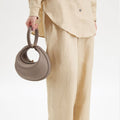 Grey full-grain leather Luna Bag with top handle and gold hardware, held by a person in a linen outfit.
