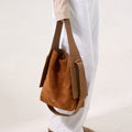 Medium Drippy Tote Bag in caramel suede with tan leather accents, worn on the shoulder by a person in white jeans.