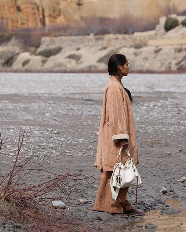 A woman in a tan outfit holds a white Medium Gather Bag Set with a beaded charm.