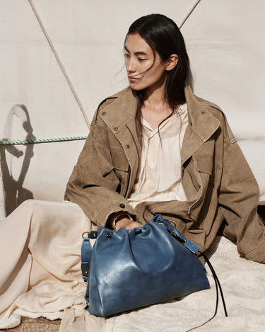 Medium Gather Bag Set in navy blue leather, featuring drawstring closure and adjustable straps. Model wearing tan jacket.