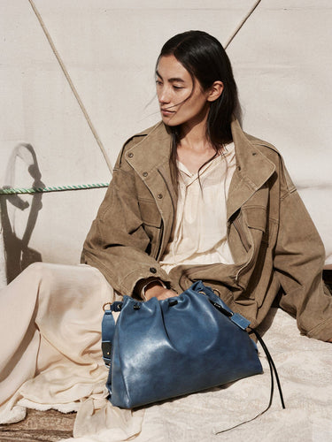 Medium Gather Bag Set in navy blue leather, featuring drawstring closure and adjustable straps. Model wearing tan jacket.