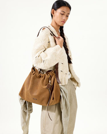 Medium Gather Bag Set in Ochre Suede with leather details, worn by a woman in a knit sweater and beige pants.