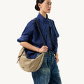 Large Luna Hobo Bag in Dune Suede with leather strap, styled by a woman in a blue shirt and jeans.