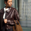 Medium Song Bag in Agarwood nubuck leather with gold hardware, carried by a woman in a brown leather jacket.