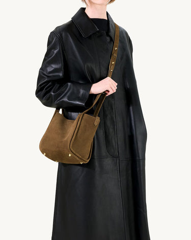 Medium Song Bag in Agarwood brown suede with gold hardware, worn by a person in a black leather coat.