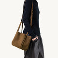 Medium Song Bag in Agarwood nubuck leather with adjustable strap, worn crossbody by a model.