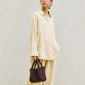 Medium Song Bag in burgundy full-grain leather with adjustable strap, carried by a woman in light yellow attire.