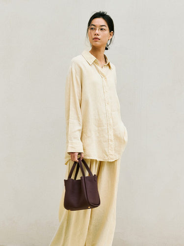 Medium Song Bag in burgundy full-grain leather with adjustable strap, carried by a woman in light yellow attire.