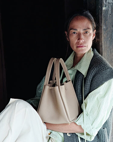 Medium Song Bag in Cream Apricot leather, held by a woman in casual attire.