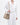 Medium Song Bag in Taupe: A pebbled leather bucket bag worn by a person in a white outfit.