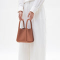 Medium Song Bag in rich, pebbled leather, held by hands in a white shirt and pants.