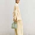 Medium Song Bag in Jade, a textured green leather handbag with double straps, held by a woman in linen attire.
