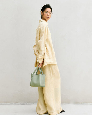 Medium Song Bag in Jade, a textured green leather handbag with double straps, held by a woman in linen attire.