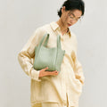 Medium Song Bag in Jade green pebbled leather, held by a woman with glasses.