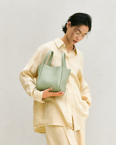 Medium Song Bag in Jade green pebbled leather, held by a woman with glasses.