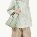 Medium Song Bag in Jade pebbled leather, carried by a person wearing a light green crinkled shirt and tan trousers.